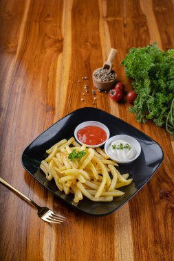 Patates kızartması ya da patates kızartması, mayonez ekşi krema ve biber sosuyla ahşap masada siyah bir tabakta.