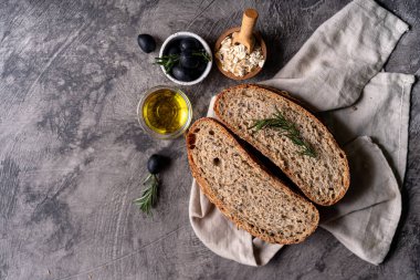 Bir ızgarada kepekli tahıllı un ve kabak tohumlarından taze pişmiş ekşi ekmek, kırsal bir ahşap masada zeytinyağı ve siyah zeytin. Esnaf ekmeği.