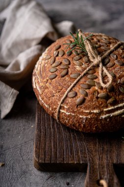 Bir ızgarada tam tahıllı un ve balkabağı tohumlarından fırınlanmış ekşi ekmek, kırsal bir ahşap masada zeytinyağı ve siyah zeytin. Esnaf ekmeği.