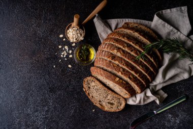 Tam tahıllı undan dilimlenmiş ekşi ekmek ve ızgarada kabak çekirdeği, kırsal bir ahşap masada zeytin yağı ve siyah zeytin. Esnaf ekmeği.