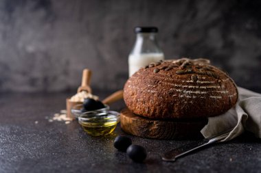 Bir ızgarada tam tahıllı un ve balkabağı tohumlarından fırınlanmış ekşi ekmek, zeytin yağı ve siyah zeytin siyah kırsal ahşap masa. Esnaf ekmeği.