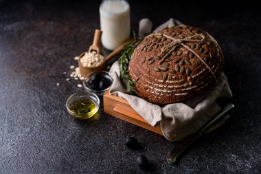 Bir ızgarada tam tahıllı un ve balkabağı tohumlarından fırınlanmış ekşi ekmek, zeytin yağı ve siyah zeytin siyah kırsal ahşap masa. Esnaf ekmeği.