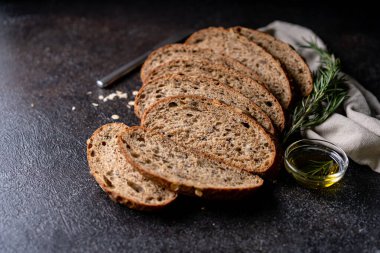 Tam tahıllı undan dilimlenmiş ekşi ekmek ve ızgarada kabak çekirdeği, kırsal bir ahşap masada zeytin yağı ve siyah zeytin. Esnaf ekmeği.