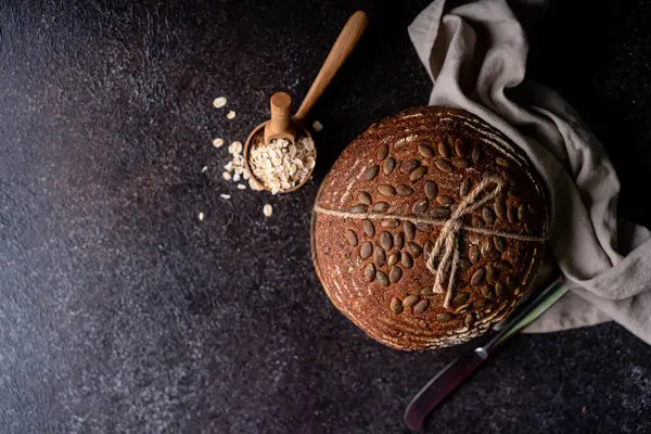 Bir ızgarada tam tahıllı un ve balkabağı tohumlarından fırınlanmış ekşi ekmek, zeytin yağı ve siyah zeytin siyah kırsal ahşap masa. Esnaf ekmeği.