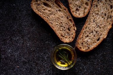 Tam tahıllı undan dilimlenmiş ekşi ekmek ve ızgarada kabak çekirdeği, kırsal bir ahşap masada zeytin yağı ve siyah zeytin. Esnaf ekmeği.