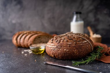 Tam tahıllı undan dilimlenmiş ekşi ekmek ve ızgarada kabak çekirdeği, kırsal bir ahşap masada zeytin yağı ve siyah zeytin. Esnaf ekmeği.