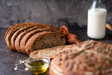 Tam tahıllı undan dilimlenmiş ekşi ekmek ve ızgarada kabak çekirdeği, kırsal bir ahşap masada zeytin yağı ve siyah zeytin. Esnaf ekmeği.