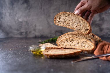 Tam tahıllı undan dilimlenmiş ekşi ekmek ve ızgarada kabak çekirdeği, kırsal bir ahşap masada zeytin yağı ve siyah zeytin. Esnaf ekmeği.