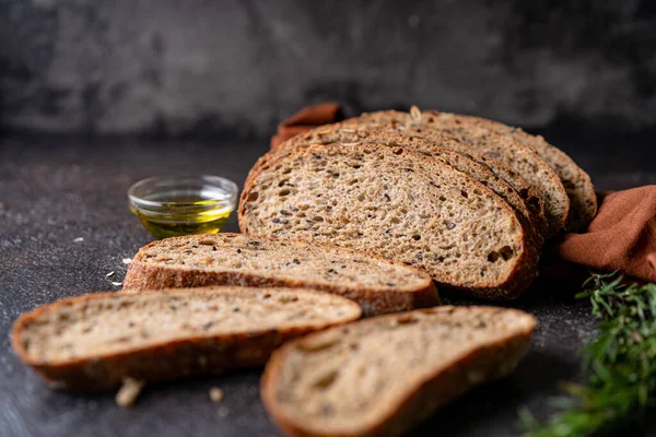 Sliced sourdough bread from whole grain flour and pumpkin seeds on a grid, olive oil and black olive on a rustic wooden table. Artisan bread.