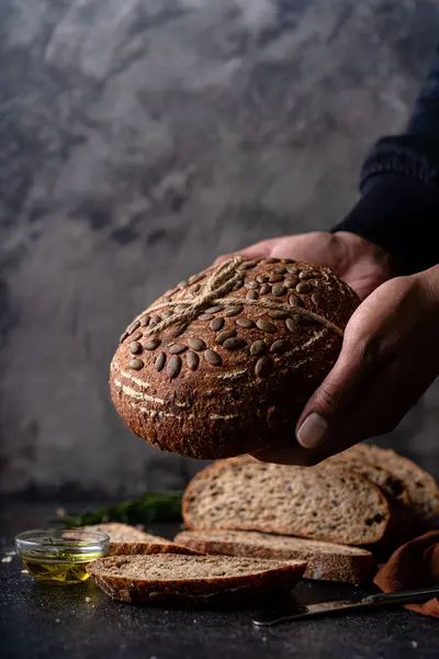 Tam tahıllı undan dilimlenmiş ekşi ekmek ve ızgarada kabak çekirdeği, kırsal bir ahşap masada zeytin yağı ve siyah zeytin. Esnaf ekmeği.