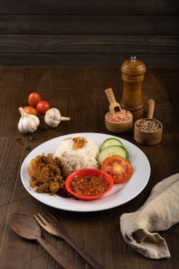 Ayam Goreng Lengkuas Kremes or Crispy Galangal Fried Chicken with steamed rice and chili paste or sambal on white plate and wood table clipart