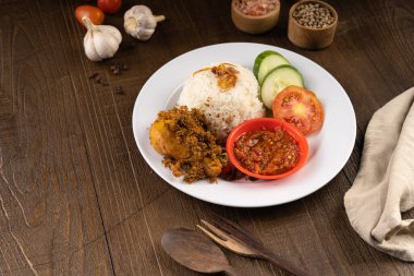 Ayam Goreng Lengkuas Kremes veya Çıtır Galangal Kızarmış Tavuk ile buğulanmış pirinç ve biber ezmesi veya beyaz tabak ve ahşap masa üzerinde sambal