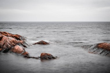 Denizde kayaların uzun pozlu görüntüsü. Ağustos ayının bulutlu bir gününde Holmon 'un kuzey kesiminde. Holmon İsveç 'te bir adadır..