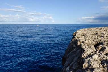 View over the ocean from a cliff as a boat sails in the distance