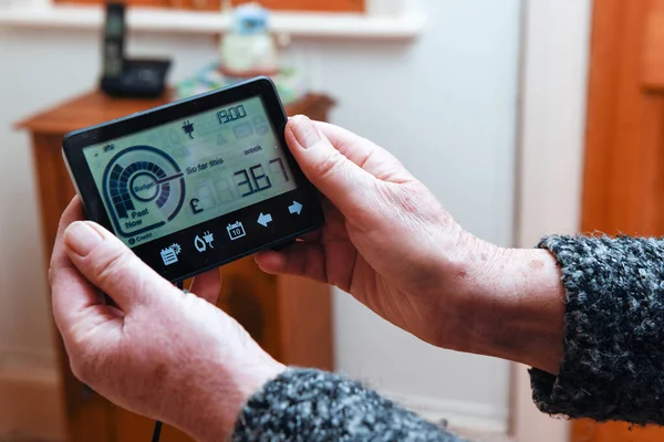 A senior woman looks at the smart meter to budget for energy bills for the household