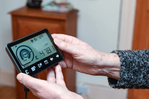 A senior woman looks at the smart meter to budget for energy bills for the household