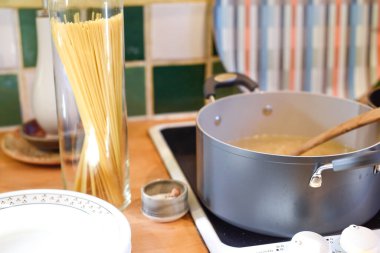 Ev mutfağında makarna pişirirken tavada spagetti ve mutfak tezgahında hammadde pişirmek için kaynar su bulunur.