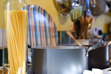 Ev mutfağında makarna pişirirken tavada spagetti ve mutfak tezgahında hammadde pişirmek için kaynar su bulunur.