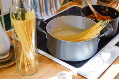 Ev mutfağında makarna pişirirken tavada spagetti ve mutfak tezgahında hammadde pişirmek için kaynar su bulunur.