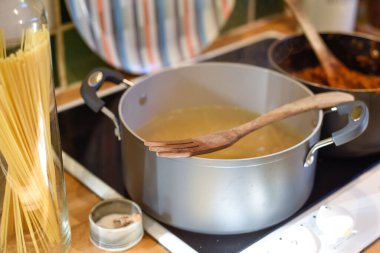 Ev mutfağında makarna pişirirken tavada spagetti ve mutfak tezgahında hammadde pişirmek için kaynar su bulunur.