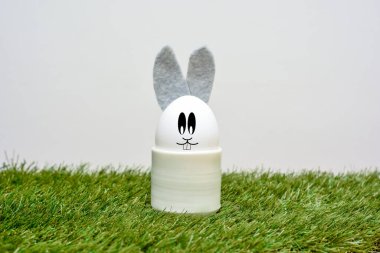 Tavşan suratlı ve kulaklı Paskalya yumurtası. Beyaz arka planda çimenlerin üzerinde.