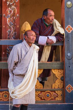 Geleneksel Gho giyen Bhutanse erkekleri yerel Tshechu 'yu izliyor.