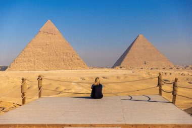 Giza Platosu 'ndaki piramitlerin genel görünümü önünde meditasyon yapan bir turist..