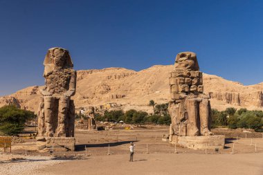 Famous two Colossi of Memnon - massive ruined statues of the Pharaoh Amenhotep III. Travel and tourist landmarks clipart