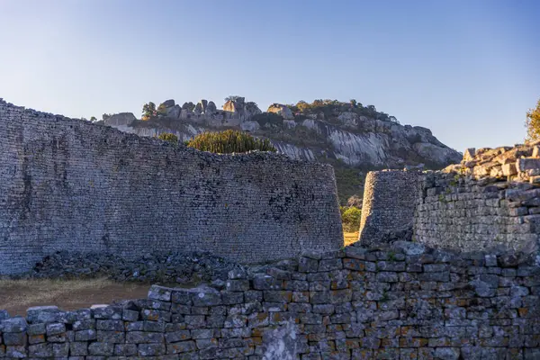 Büyük Zimbabwe harabelerinin manzarası ön planda büyük bir muhafaza ve tepe kompleksi yükseliyor. Eski Afrika medeniyetinin güçlü bir sembolü..