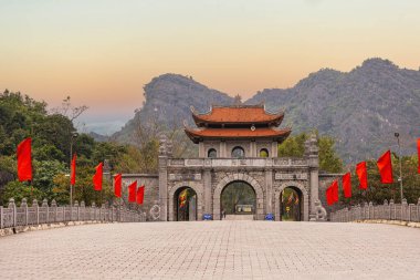 Vietnam 'ın Ninh Binh şehrinde geleneksel bir taş kapı. Yeşillik ve kireçtaşı karistiyle çevrelenmiş portal, Vietnam mimari mirasını yansıtan tarihi veya ruhani bir sitenin girişini gösteriyor..