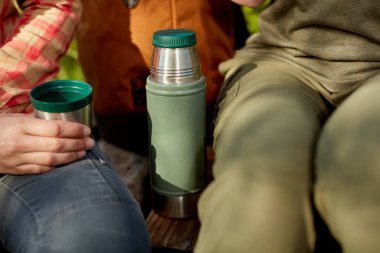 Termal şişeden bir kupa sıcak kahve içen bir kadın açık havada bir arkadaşıyla yakın planda sohbet ederken...