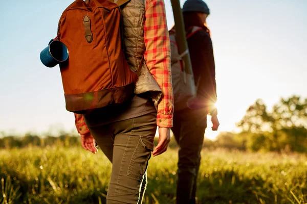 stock image Two fit young women on an early morning hike walking through a field with their backpacks lit by a sunburst of the rising sun