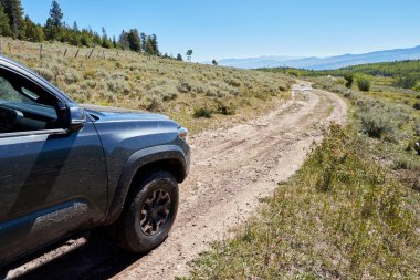 4WD aracı dar bir toprak yolda manzaralı dağ manzarası boyunca ilerliyor. Ön taraftaki yakın çekim manzarası çevreye bakıyor.