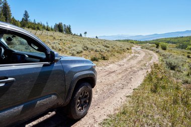 4WD aracı bir off road yaz tatili sırasında dar virajlı toprak bir yol boyunca dağ manzarasından geçiyor.