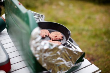 Dışarıdaki gaz ocağında hamburger köftesi pişirmek. Folyo rüzgâr korumaları da kamp yaparken taşınabilir küçük bir çantaya yerleştirilmiş.