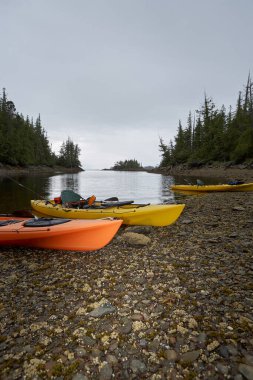 Akşam ışığında sakin su ve ön planda fotokopi alanı olan taşlı bir sahilde kanolar karaya vurdu.