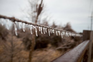 Buz saçakları kırsal kesimde soğuk ve gri bir kış gününde tel ya da ipten sarkıyor.