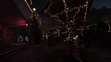 Kasaba meydanında güzel bir kış gecesi. Pazar, tezgahlarda gezinen ve festival atmosferinin tadını çıkaran insanlarla dolu. Her yerde Noel ağaçları, ışıklar ve süslemeler var. A