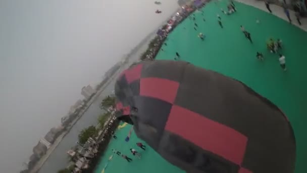 视频从热气球下降时的特写开始 显示它的黑色和红色 以及背景中的人和风筝 当气球继续下降时 摄像机 — 图库视频影像