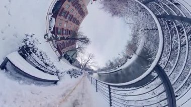 Bu, şehir parkındaki karlı bir yolun 360 derecelik bir videosu. Yol ağaçlar ve çalılarla çevrili ve sağda bir çit var. Kar zeminde yoğun ve ağaçlar çıplak. Öyle.