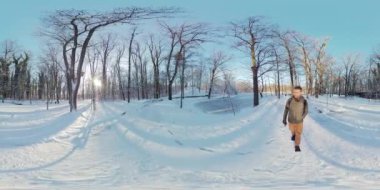 Bu 360 derecelik video karlı bir ormanda yürüyen bir adamı gösteriyor. Adam sıcak bir kışlık ceket ve şapka giyiyor. O bir sırt çantası taşıyor ve karla kaplı bir yolda yürüyor. Ormandaki ağaçlar