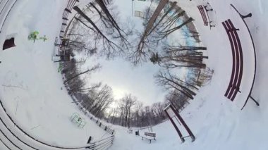 Bu, kışın karlı bir parkın 360 derecelik görüntüsü. Video, karla kaplı ağaçlar, banklar ve patika olan bir park gösteriyor. Video yerden çekilmiş ve parkın tam bir görüntüsünü sağlıyor.