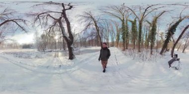 Bu, karlı bir ormanda yürüyen bir adamın 36 derecelik videosu. Adam siyah bir ceket, gri pantolon ve kahverengi ayakkabılar giyiyor. O kahverengi bir çanta taşıyor. Orman karla kaplı.