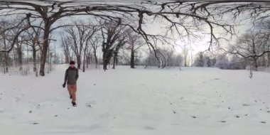 Bu, kışın karlı bir ormanda yürüyen bir adamın 360 derecelik videosu. Adam sıcak bir kışlık ceket ve şapka giyiyor ve bir sırt çantası taşıyor. Karla kaplı bir yolda yürüyor ve...