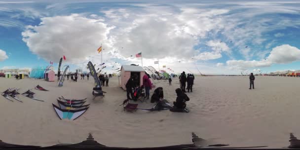 ビーチでカイトフェスティバルの360度ビデオ ビデオは 小さなピンクの建物と空を飛んでいるいくつかのカラフルなキットを持つ広い砂浜を示しています 歩いている人もたくさんいます — ストック動画