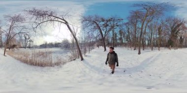 Video, karlı bir ormanda yürüyen bir adamın 360 derecelik sanal gerçeklik deneyimi. Adam siyah bir ceket ve kahverengi pantolon giyiyor ve bir sırt çantası taşıyor. Karda yürüyor.