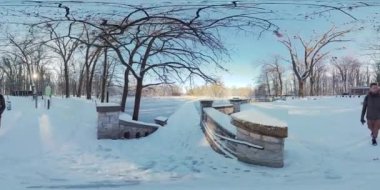 Video, kışın karlı bir parkta yürüyen bir adamın 360 derecelik sanal gerçeklik videosu. Adam siyah bir ceket ve gri bir eşarp giyiyor. Karla kaplı bir yolda yürüyor.