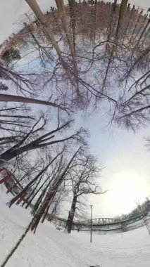 Video, kışın karlı bir parkın 360 derecelik görüntüsüyle açılıyor. Park karla kaplı ve ağaçlar çıplak. Uzakta bir köprü var. Parkta bir kişi yürüyor ve...