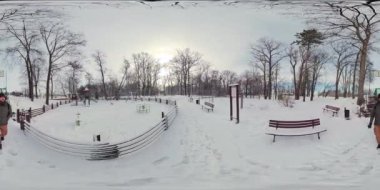 Video, karlı bir parkın 360 derecelik görüntüsüne açılıyor. Park beyaz karla kaplı ve parkların çevresini çevreleyen birkaç ağaç ve çalılık var. Orada bir çocuk parkı var.