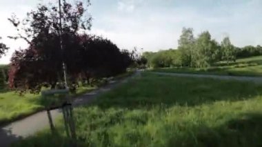 Burası bir sürü ağacı, yolu ve bankı olan güzel bir park. Park çok yeşil ve yemyeşil ve ağaçlar tamamen çiçek açmış. Yol betondan yapılmış ve ağaçlarla kaplı. Bankta.